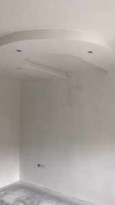 Leerer Raum mit abgehängter Decke in Kurvenform, eingebauten Leuchten, sichtbaren Kabeln und Rohbetonboden