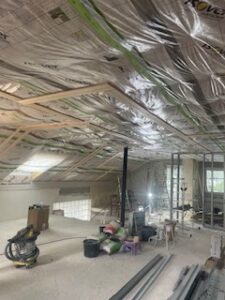 Renoviertes Dachgeschoss mit installierter Dämmung, sichtbaren Holzbalken, Werkzeugen, Materialsäcken und Tageslicht