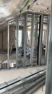 Baustellenraum mit Metallständerwand, grünem Dämmmaterial an der Decke, Leiter und Werkzeugen