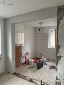 Halbrenovierter Raum mit weißer Fliesenwand, offenliegenden Wasserleitungen, Werkzeugen und natürlichem Lichteinfall