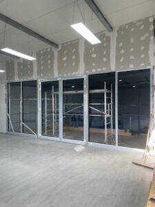 Baustellenraum mit vier großen Glastüren, Metallrahmen, Trockenbauwänden, Gerüst und Betonboden