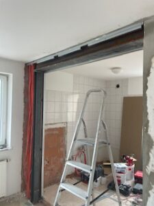 Renovierungsraum mit montiertem Metallsturz über Maueröffnung, Leiter, freiliegender Verkabelung und Werkzeugen