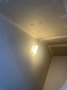 Raum in Renovierung mit gespachtelter Decke, sichtbaren Unebenheiten, Wandlampe mit vier Strahlern und grober Wandtextur